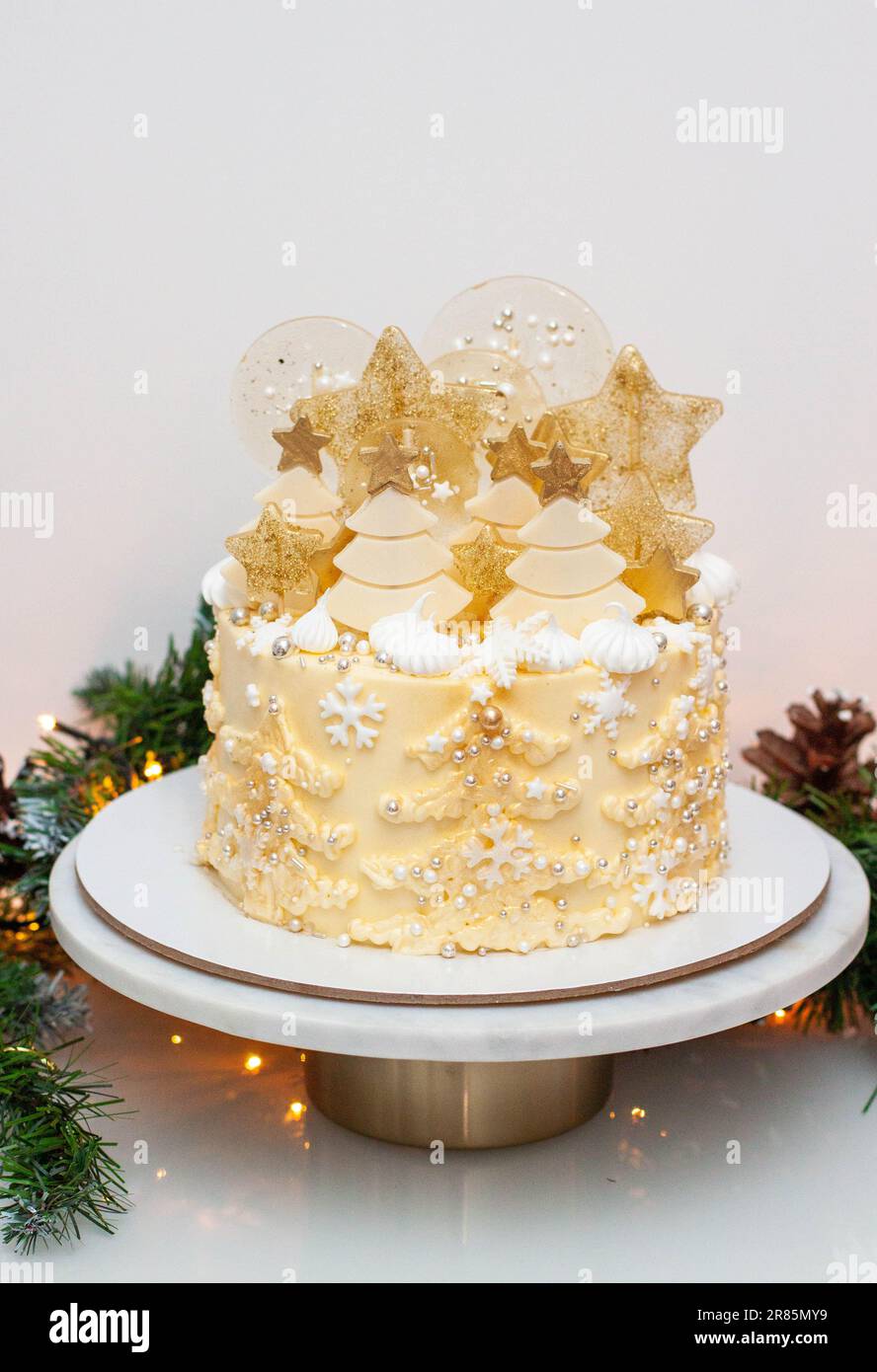 Gâteau de noël doré et blanc de fête avec arbres de noël crémeux, sucettes, flocons de neige fondants, décoration chocolat, paillettes et arrosettes Banque D'Images