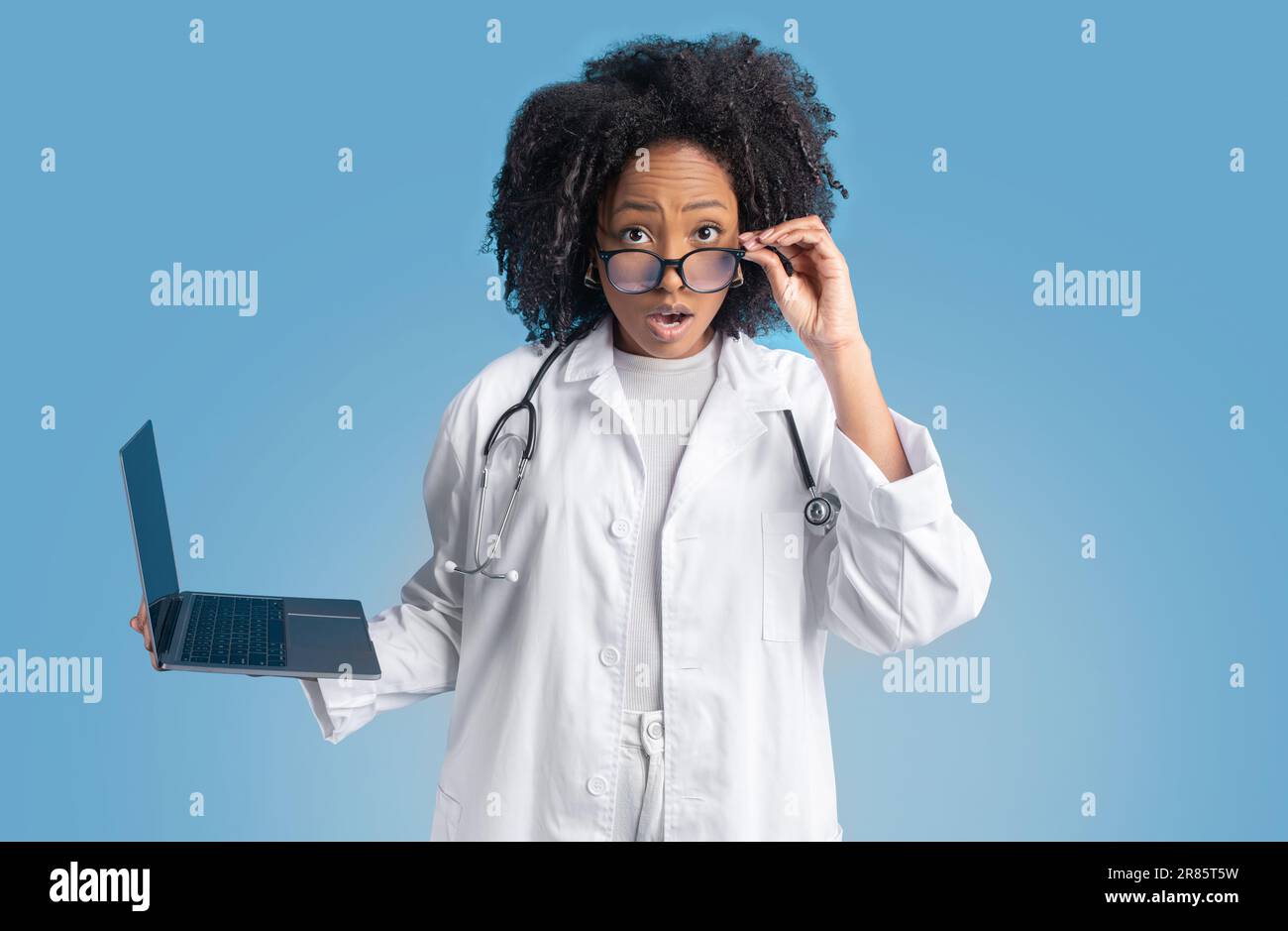 Choqué jeune afro-américaine maurille femme médecin thérapeute en manteau blanc avec ordinateur portable prend des lunettes Banque D'Images