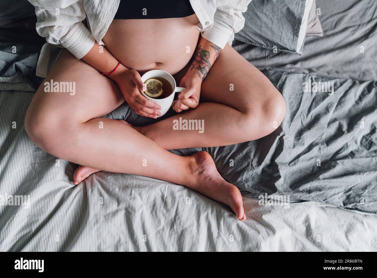 Jeune femme enceinte assise avec pattes croisées sur le lit. Tasse de thé photo dans la chambre en début de matinée. La santé de la femme, heureux prougn Banque D'Images