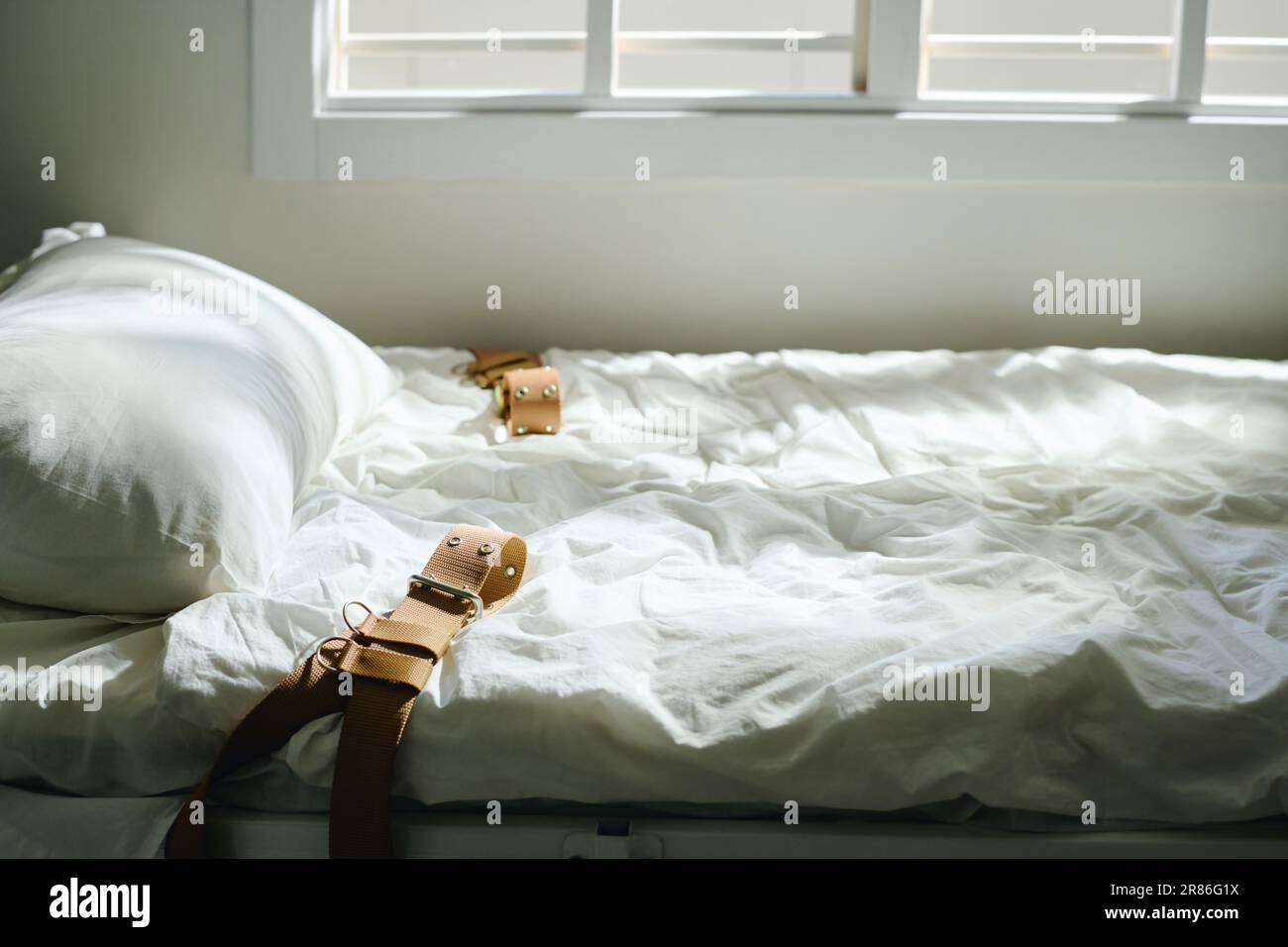 Vue latérale du lit avec drap propre, oreiller et quatre ceintures serrées  préparées pour les patients fous debout près de la fenêtre dans la salle  d'hôpital mentale Photo Stock - Alamy