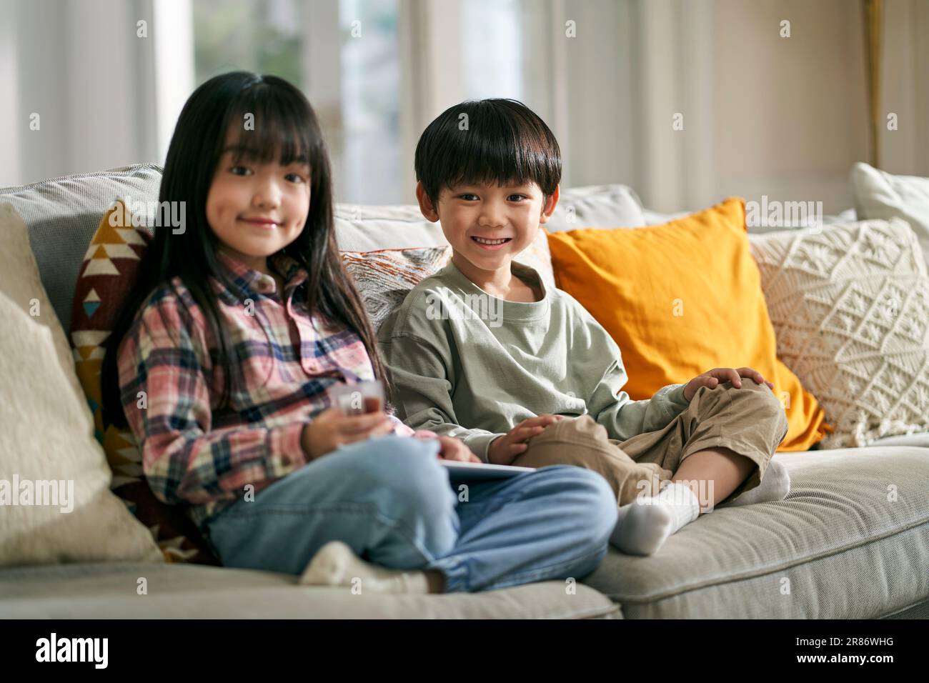 portrait de deux enfants asiatiques frère et soeur assis sur un canapé de famille à la maison regardant l'appareil photo sourire Banque D'Images