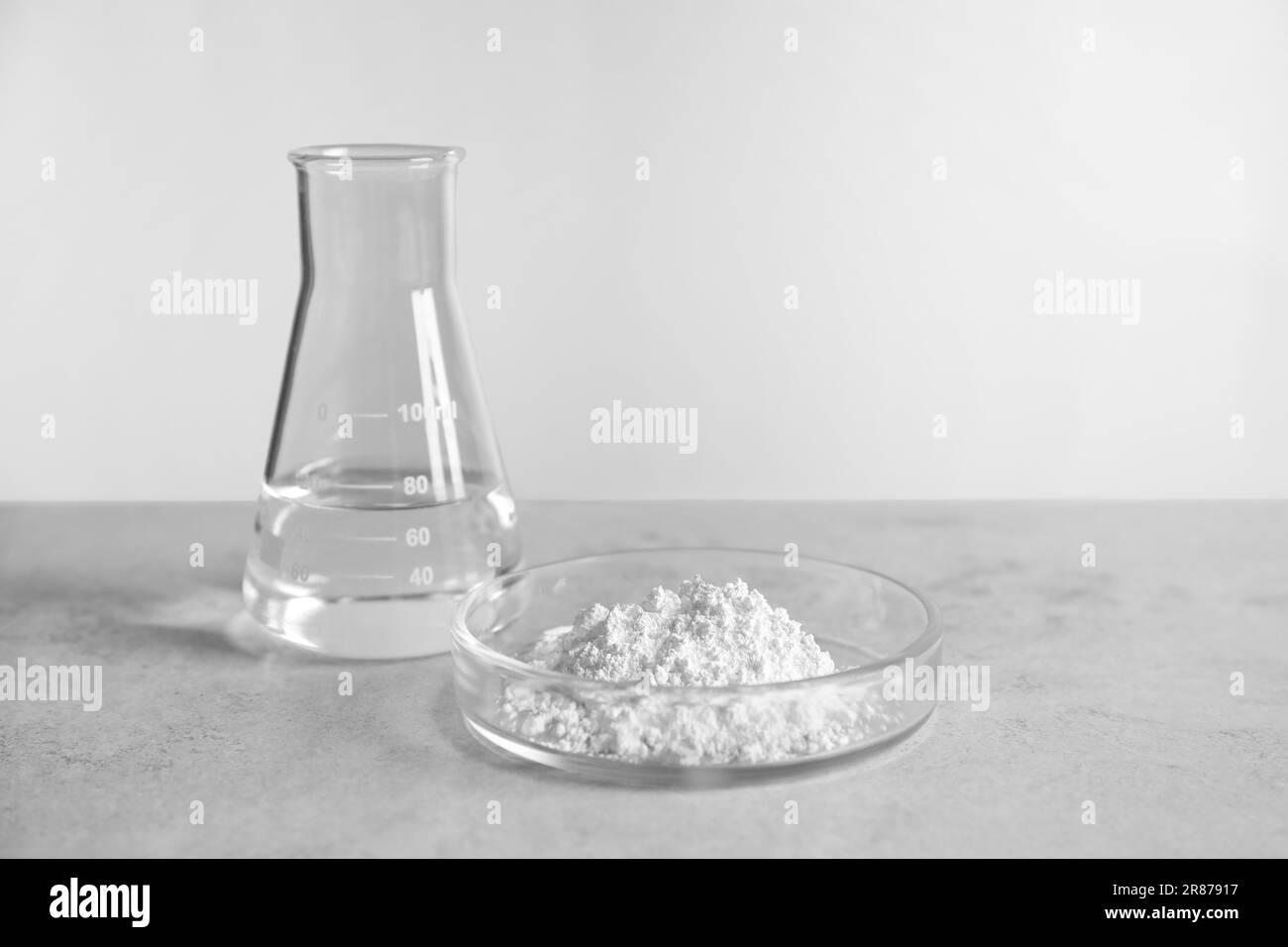 Boîte de Pétri avec poudre de carbonate de calcium et flacon de laboratoire sur table gris clair. Espace pour le texte Banque D'Images