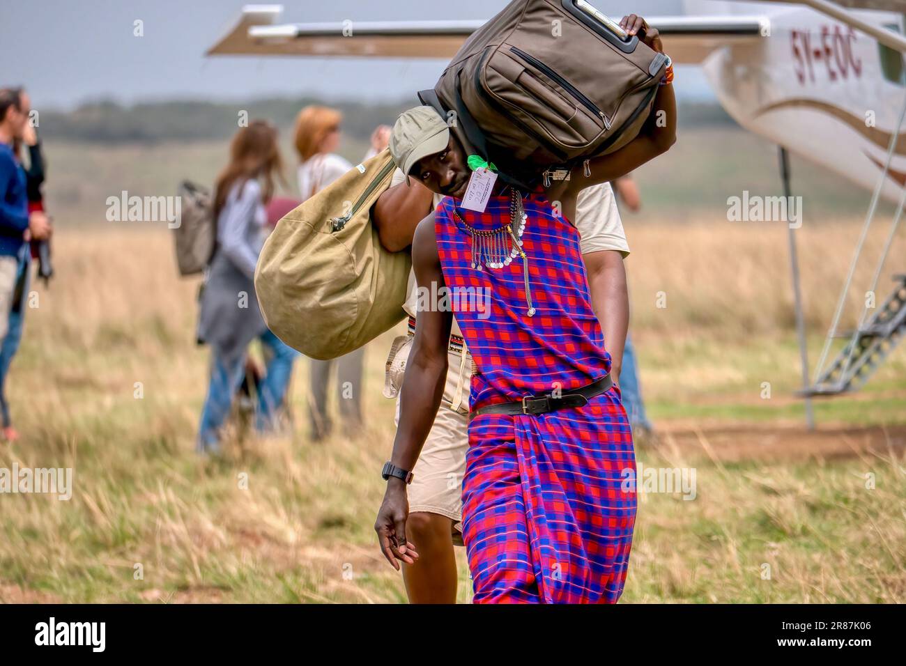 Maasai Mara, Kenya - 25 septembre 2013. Un membre de la tribu Maasai employé par un camp de safari transporte les bagages passagers d'un vol charter. Banque D'Images