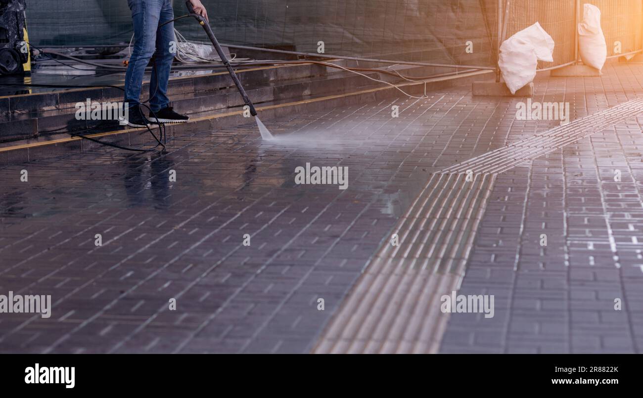 Nettoyage du sol extérieur avec jet d'eau haute pression. le personnel de nettoyage tuyau une voiture portable pour laver le sol en béton Banque D'Images