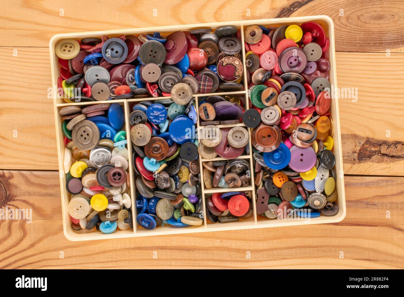 Plusieurs boutons dans un conteneur en plastique sur une table en bois, macro, vue de dessus. Banque D'Images