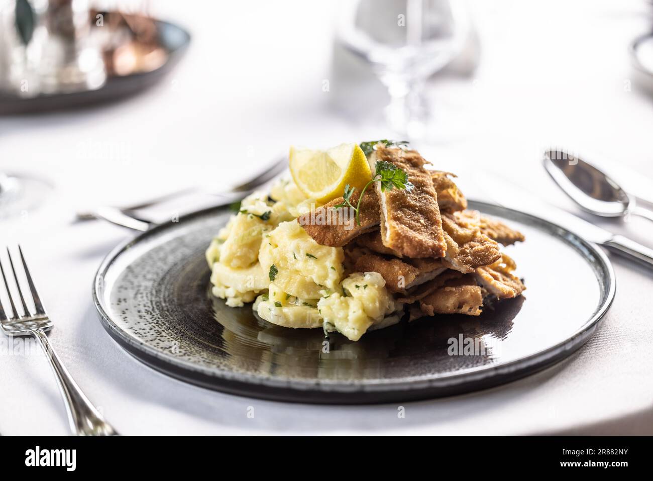 Orecchio d'elefante coupé en tranches et servi sur une salade de pommes de terre avec un coin de citron. Banque D'Images