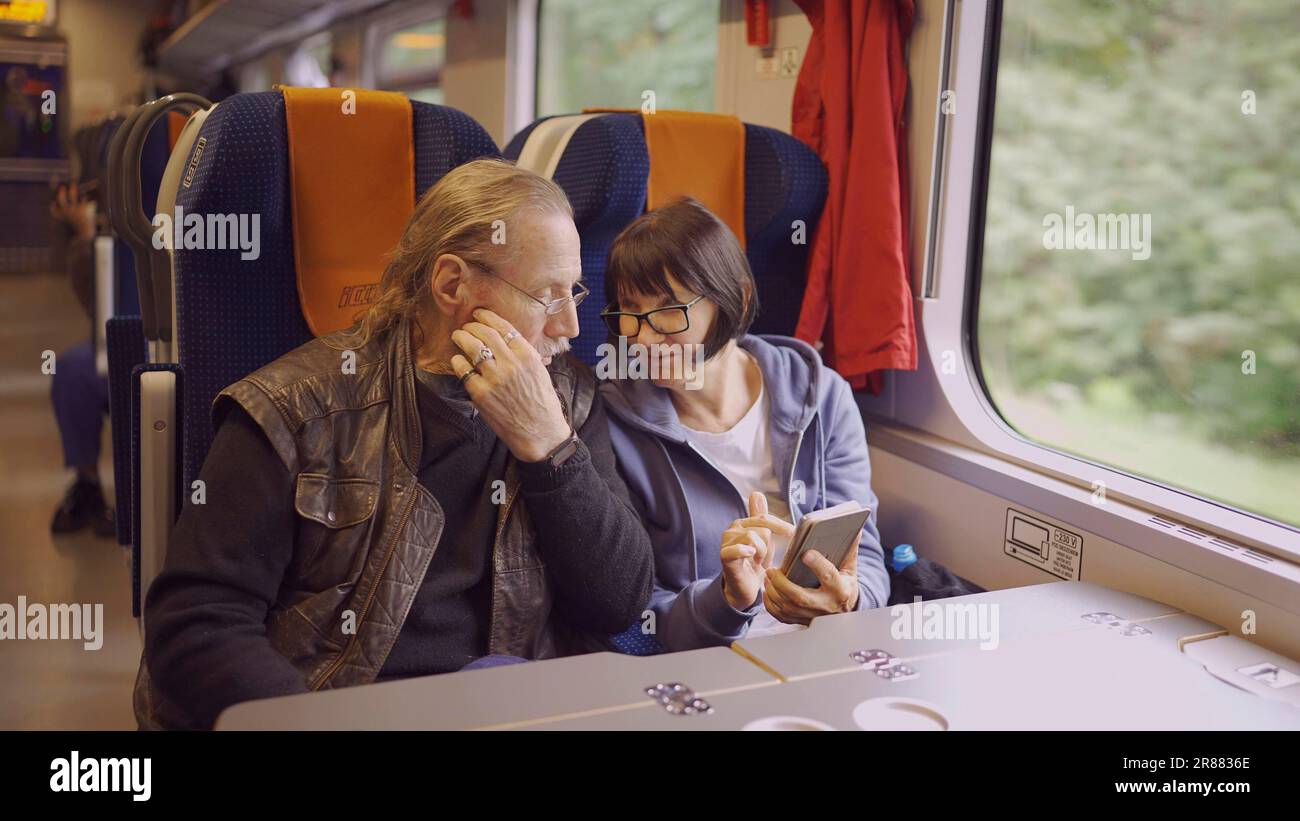 Un couple âgé voyage en train, la dame tient un téléphone portable dans sa main, les deux regardent le smartphone et parlent l'un avec l'autre Banque D'Images