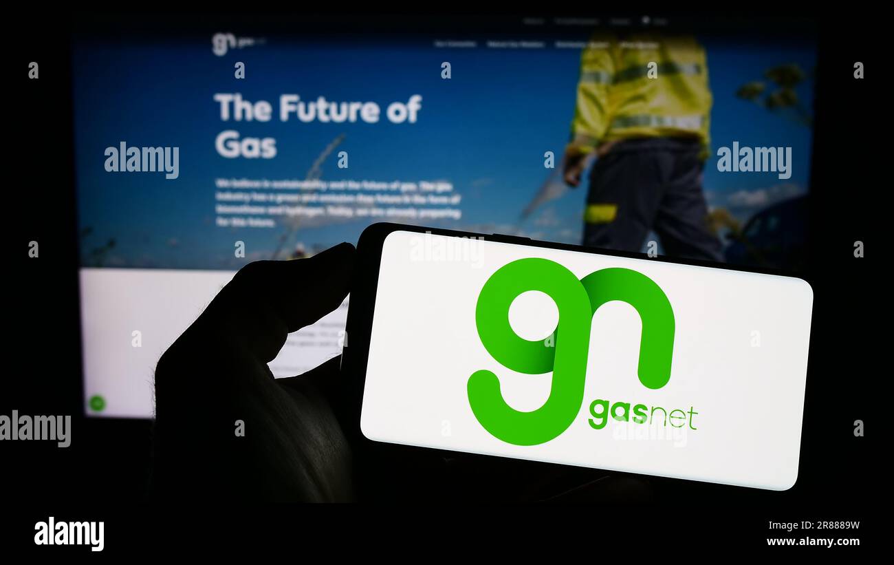 Personne tenant un téléphone portable avec le logo de la société de distribution de gaz Tchèque GasNet sro sur l'écran en face de la page web d'affaires. Mise au point sur l'affichage du téléphone. Banque D'Images