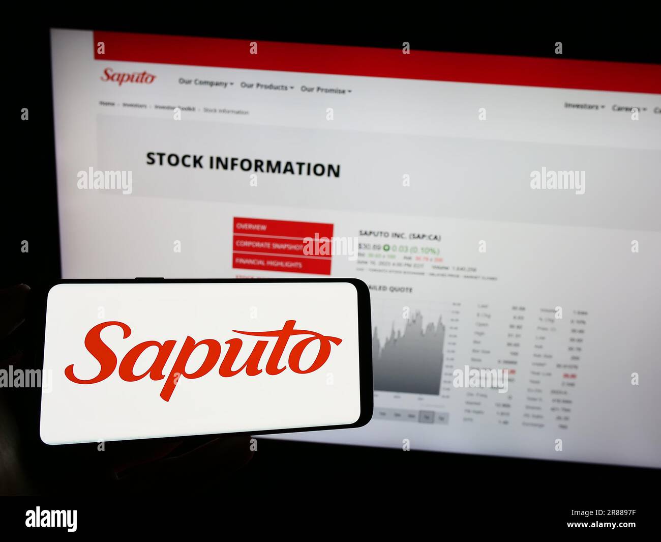 Personne tenant un téléphone portable avec le logo de la société laitière canadienne Saputo Inc. À l'écran devant la page Web d'affaires. Mise au point sur l'affichage du téléphone. Banque D'Images