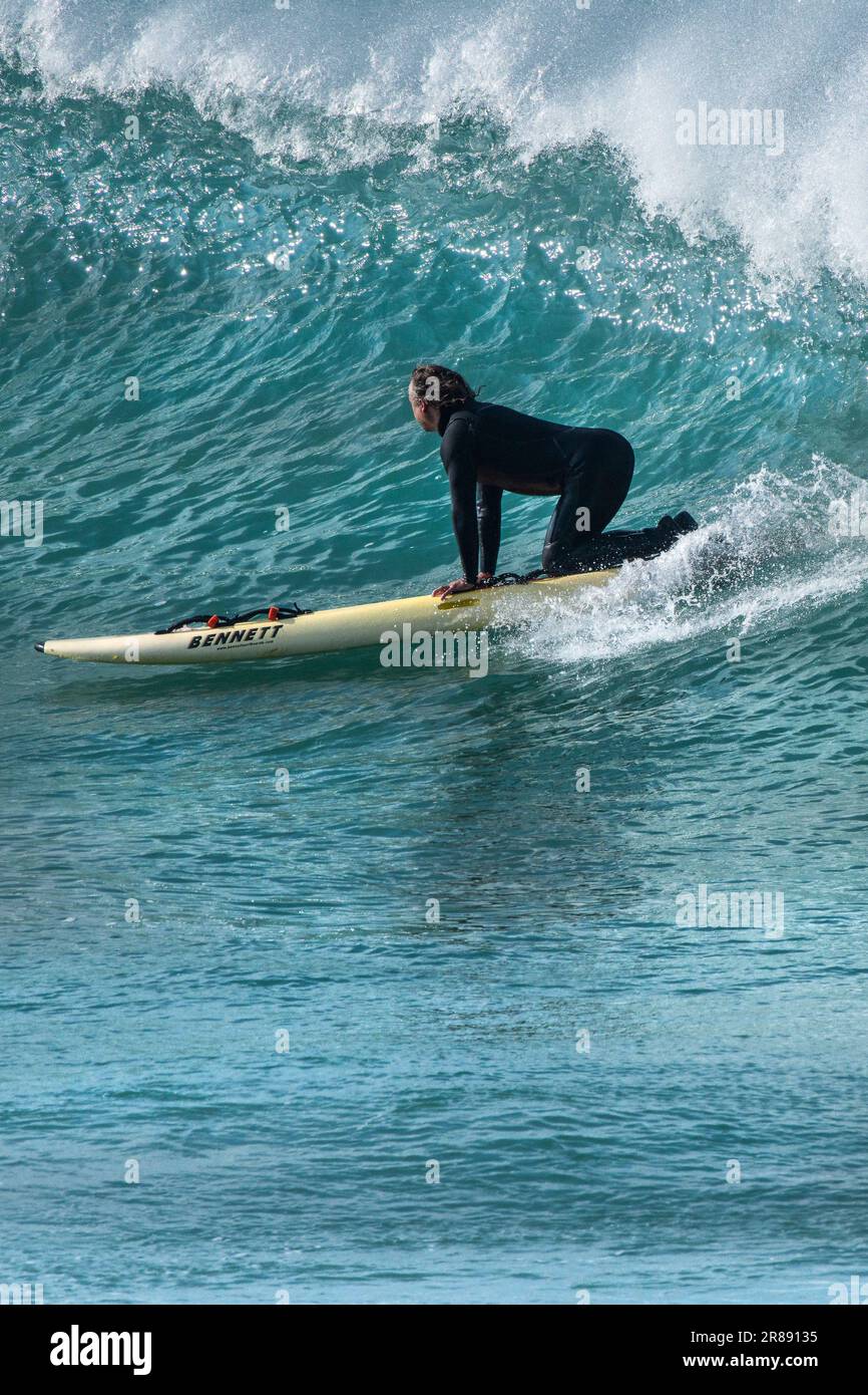 Un surfeur mûr s'agenouillant sur un Bennett Rescue Board qui fait une vague à Fistral, à Newquay, en Cornouailles, au Royaume-Uni. Banque D'Images