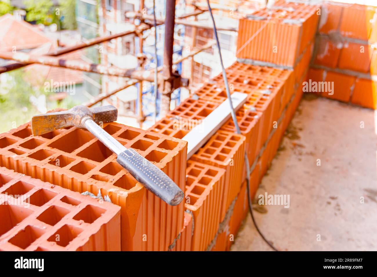 Marteau de maçon utilisé placé sur bloc de céramique rouge, mur de briques de construction. Banque D'Images