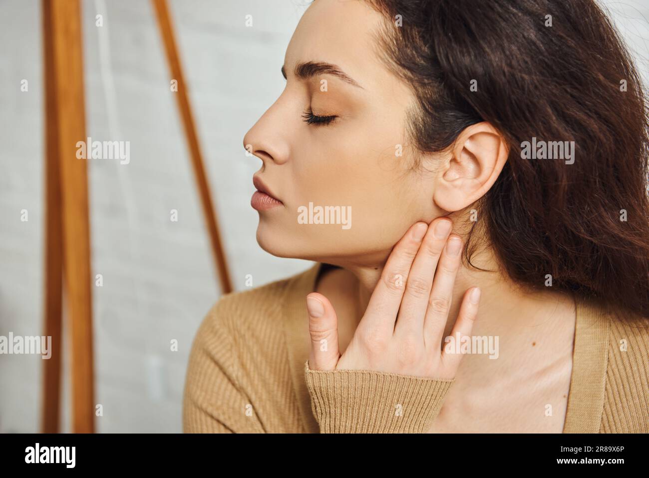 Vue latérale de la jeune femme brunette dans le visage de massage brun de  cavalier pour le soutien du système lymphatique et le drainage à la maison,  le rituel d'auto-soin et la