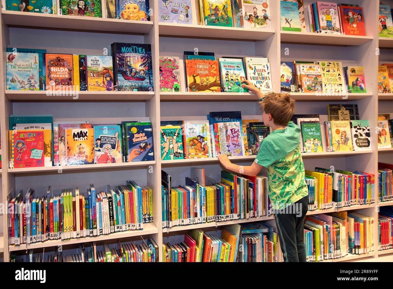 Pays-Bas, boy fait une sélection à partir d'une étagère de livres dans une bibliothèque publique. Banque D'Images