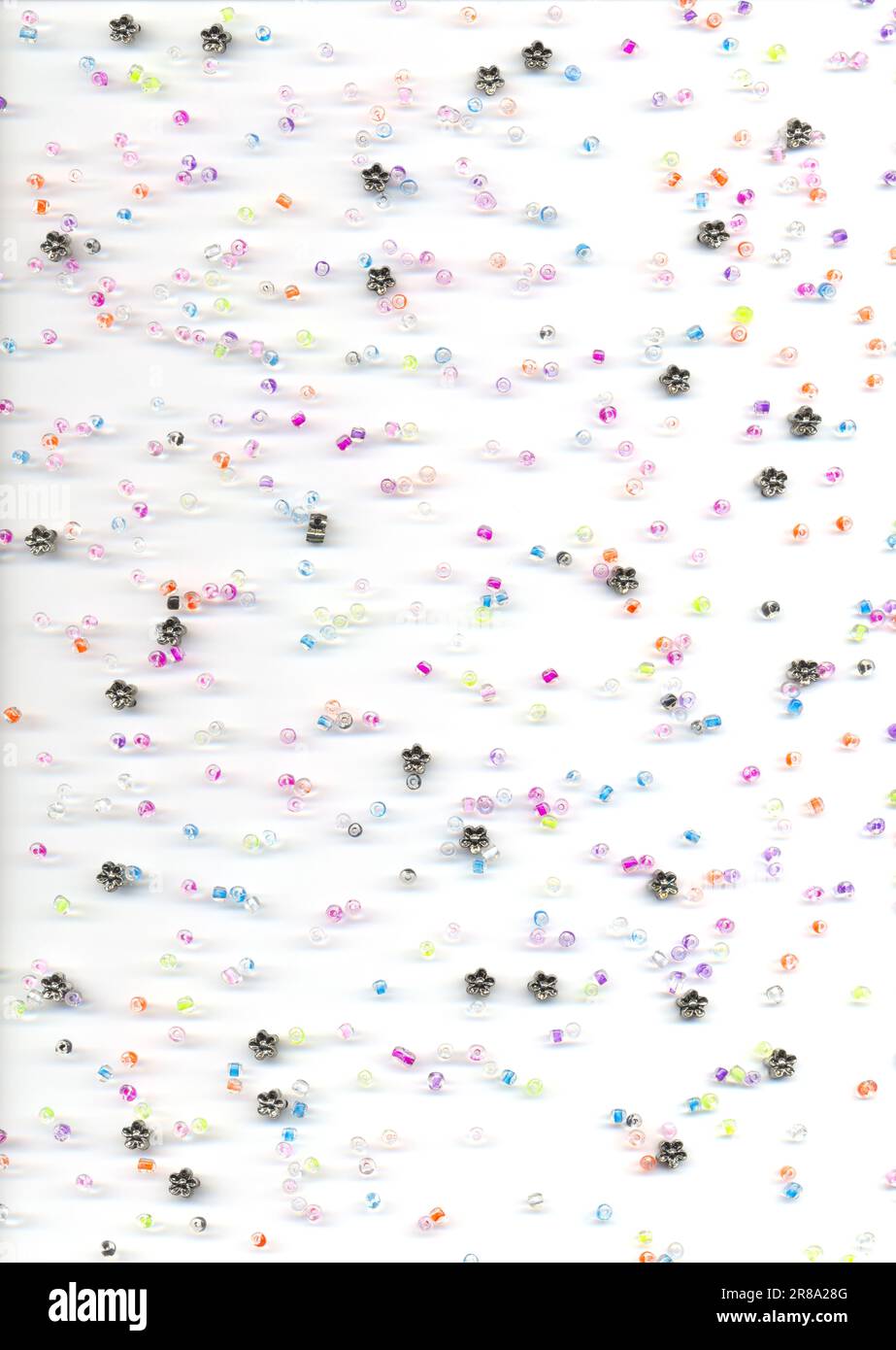 Perles de verre et de fleur colorées dispersées sur un fond blanc, vue du dessus. Fournitures d'artisanat pour les enfants passe-temps de fabrication de bijoux Banque D'Images