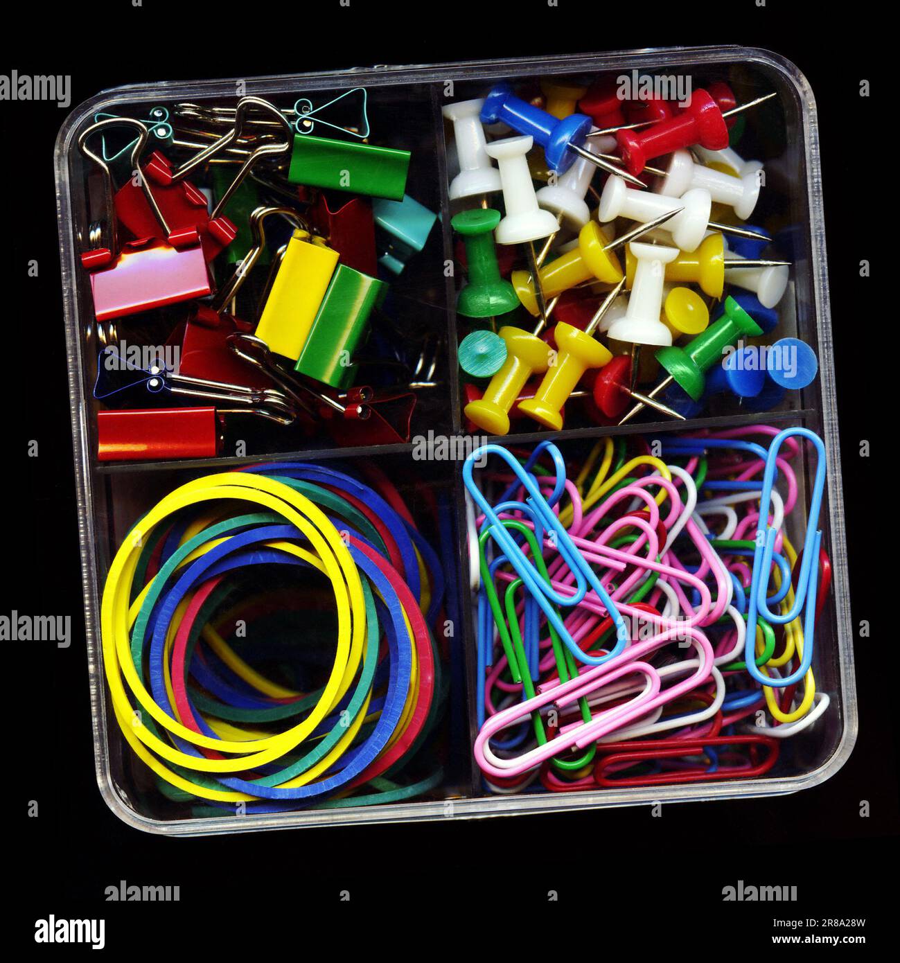 Jeu de papeterie coloré, punaises, clips, bandes en caoutchouc, pinces isolées sur le noir. Plusieurs fournitures de bureau dans une boîte en plastique en gros plan Banque D'Images
