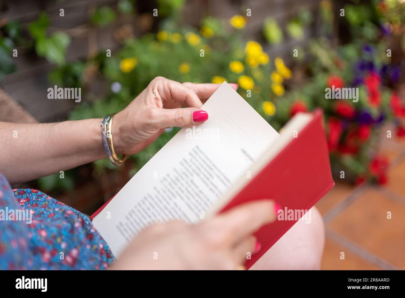 Femme lisant un livre dans le jardin avec des plantes aux fleurs de différentes couleurs. Banque D'Images