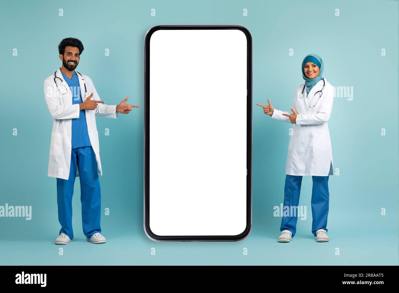 Souriant médecins musulmans en uniforme pointant les doigts sur l'écran de smartphone Big Blank Banque D'Images