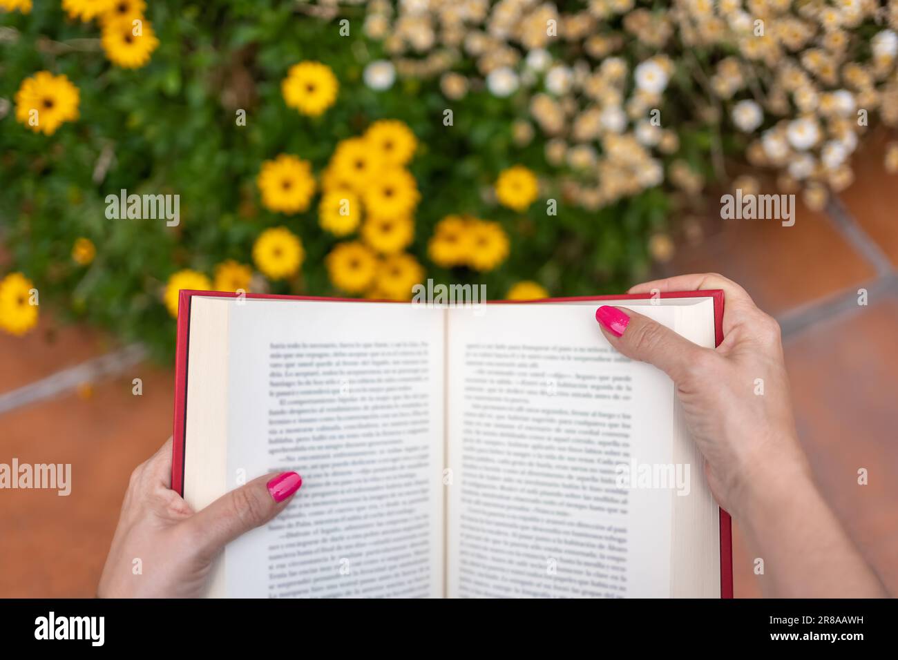 Les mains de la femme sur un livre en lisant dans le jardin à côté des plantes à fleurs. Banque D'Images