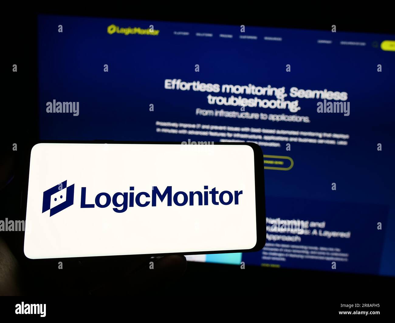 Personne tenant un téléphone mobile avec le logo de la société américaine de surveillance LogicMonitor Inc. À l'écran en face de la page Web. Mise au point sur l'affichage du téléphone. Banque D'Images
