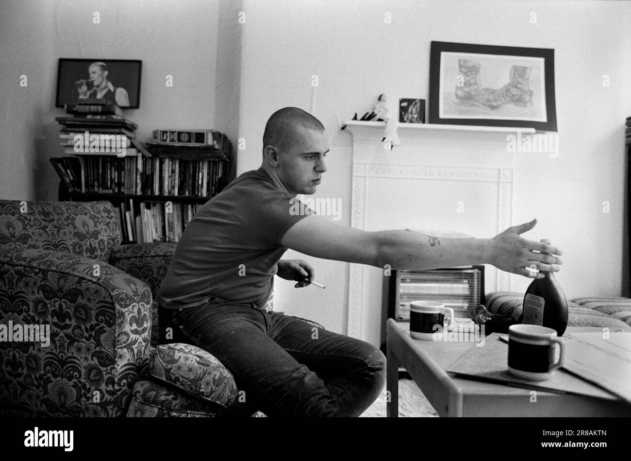 Skinhead Jimmy John (19 ans) à la maison dans un appartement du conseil Tower Hamlets. Il avait une amie française et boit du vin rose Mateus très populaire à l'époque. Le dessin sur le manteau est de lui. Il travaille comme porteur de déchets à l'hôpital Royal London Hospital Whitechapel. Londres, Angleterre 1980. ANNÉES 1980 ROYAUME-UNI HOMER SYKES Banque D'Images