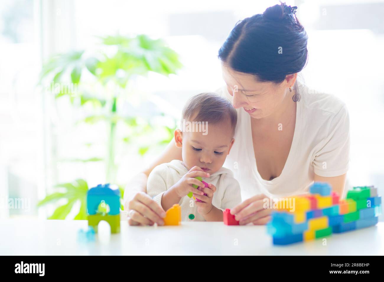 Mère asiatique et bébé garçon jouant avec des blocs colorés jouet dans la chambre blanche ensoleillée. Maman et bébé avec des jouets éducatifs. Tour de bâtiment pour enfants. Banque D'Images