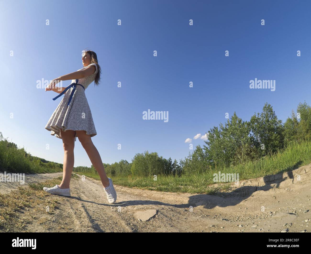 Une fille en forme danse dehors dans une robe florale sous le ciel ensoleillé Banque D'Images
