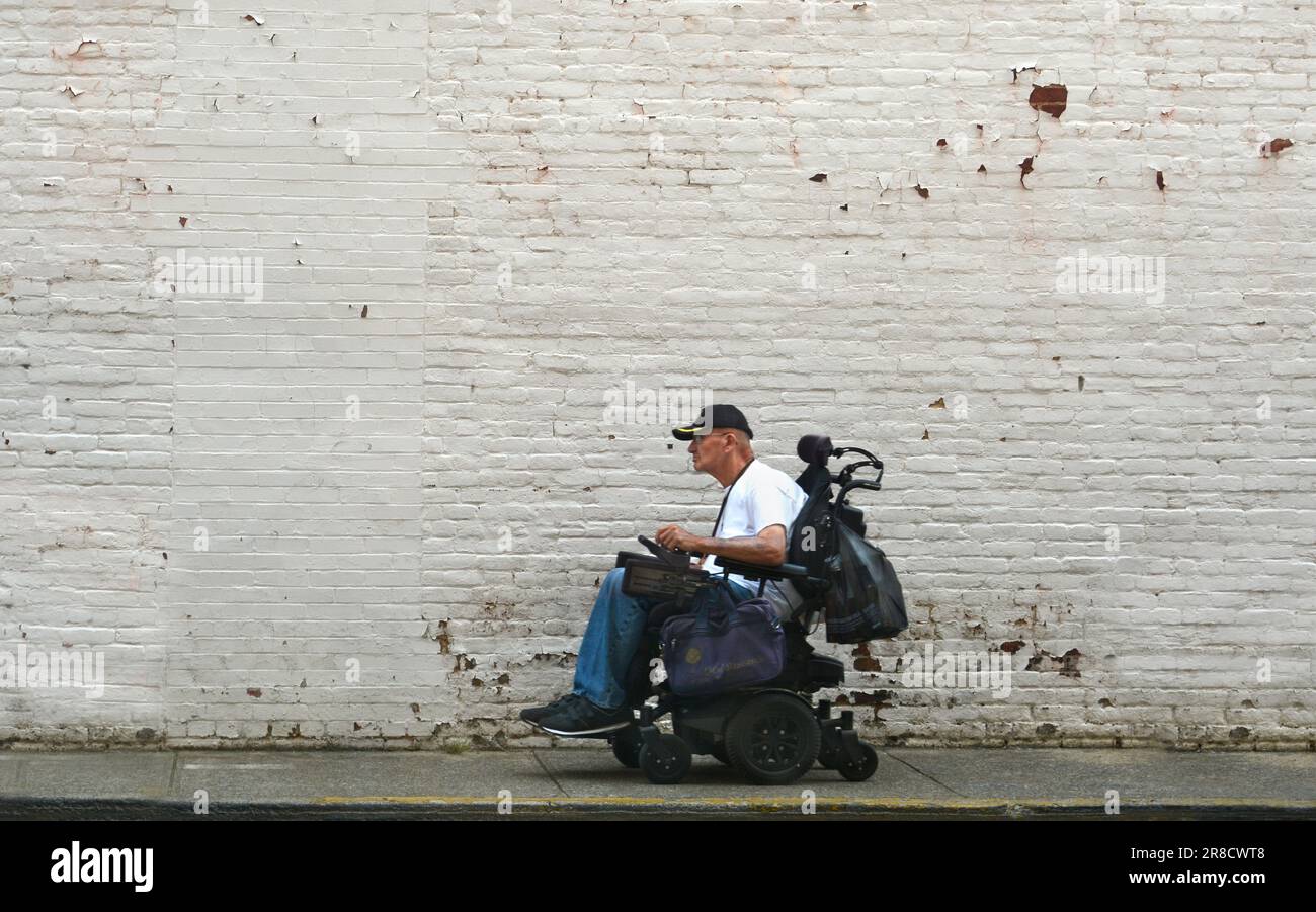 Un homme roule en fauteuil roulant motorisé, ou en fauteuil roulant motorisé, le long d'un trottoir à Bristol, en Virginie. Banque D'Images
