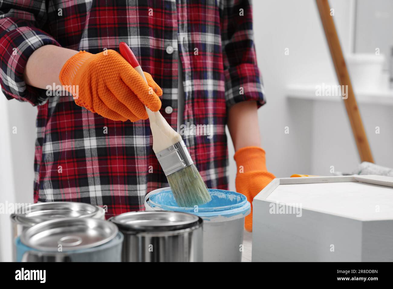 Femme plongeant la brosse dans un seau de peinture bleu clair à l'intérieur, gros plan Banque D'Images