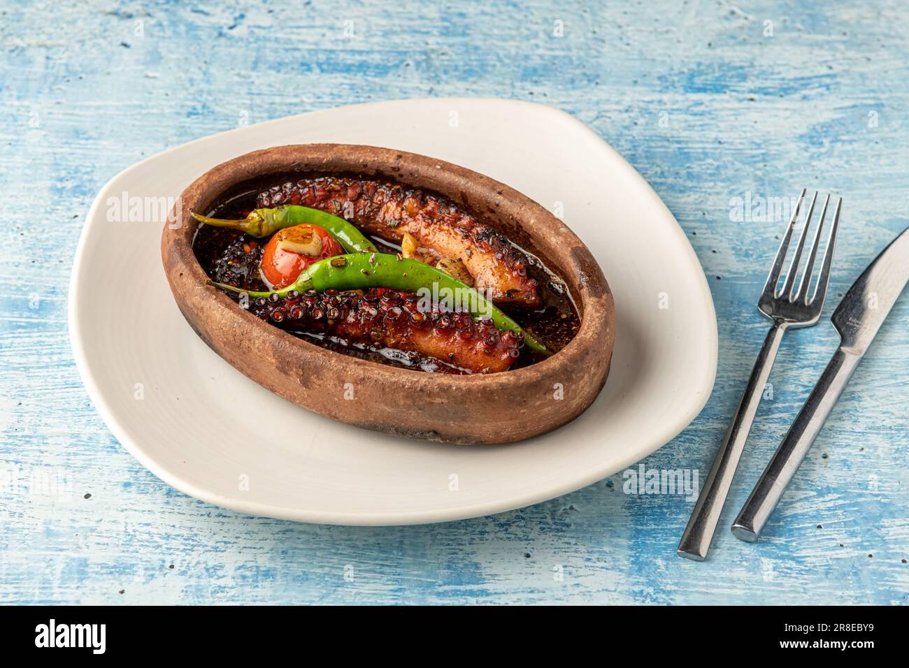 Cocotte de poulpe avec tomates et poivrons sur fond de pierre bleue Banque D'Images