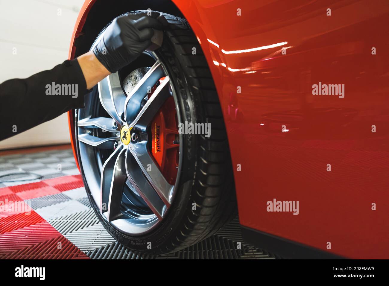 05.17.2023 Varsovie, Pologne. Main dans le gant en utilisant des produits professionnels pour noircir les pneus de Ferrari rouge. Concept de détail de voiture. Gros plan à faible angle. Photo de haute qualité Banque D'Images