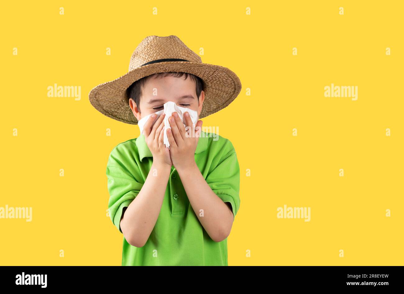 Enfant dans le chapeau soufflant dans la lingette souffrant des symptômes de la grippe sur fond jaune. Banque D'Images