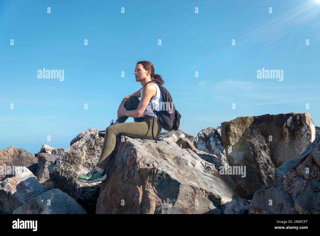 Marcheur féminin assis à un sommet rocheux en profitant de la vue au-dessus des nuages. Banque D'Images