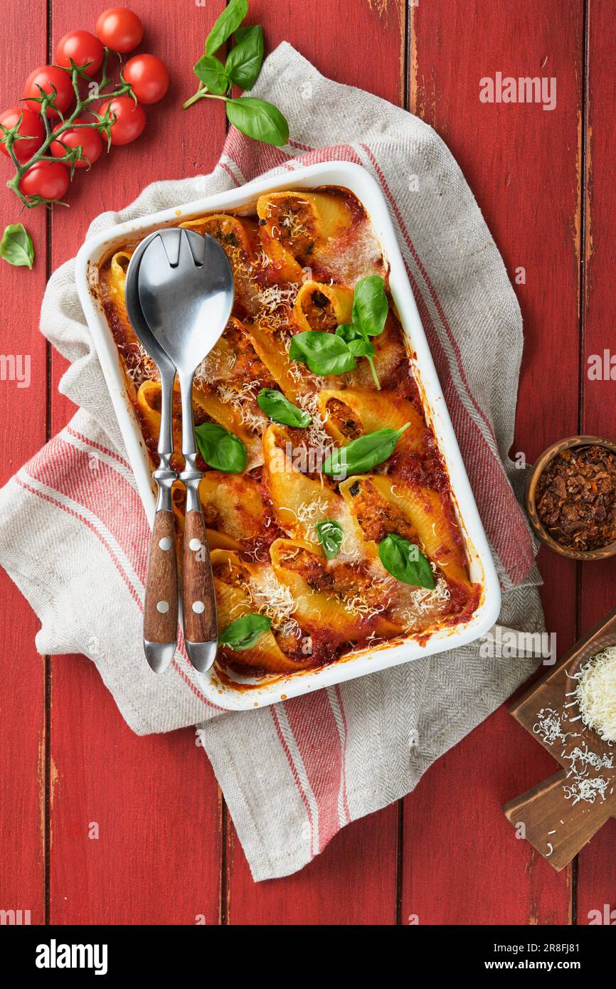 Cannelloni ou conchiglioni. Pâtes farcies cuites à la sauce à la viande bolognaise, tomates, basilic sur une table rustique en bois rouge. Bolo italien traditionnel Banque D'Images