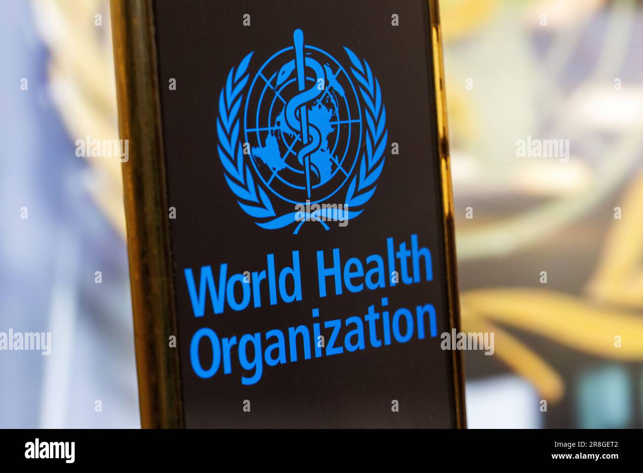 Image de symbole : smartphone avec logo DE L'OMS (Organisation mondiale de la Santé) sur fond flou Banque D'Images