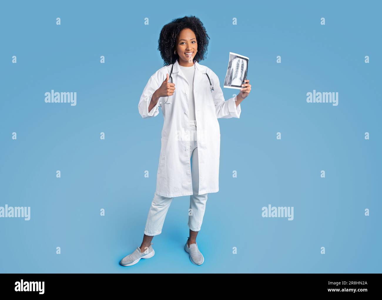 Bonne jeune afro-américaine curly femme médecin thérapeute en manteau blanc faire signe pouce vers le haut, montrer la radiographie Banque D'Images