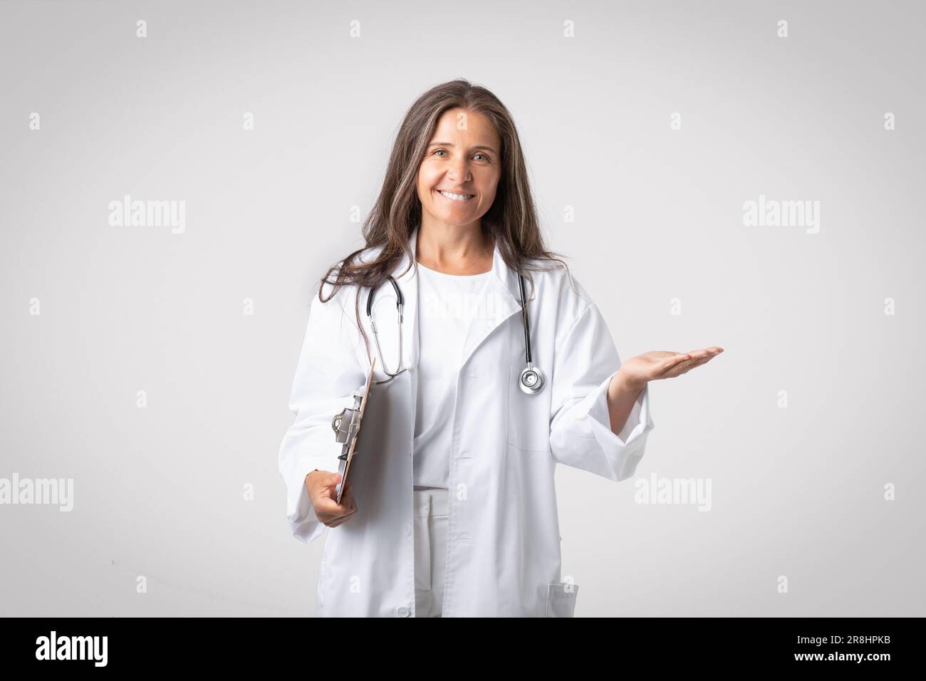 Femme âgée excitée médecin tenant le presse-papiers et montrant quelque chose sur la paume vide, la publicité de poduit ou la clinique Banque D'Images