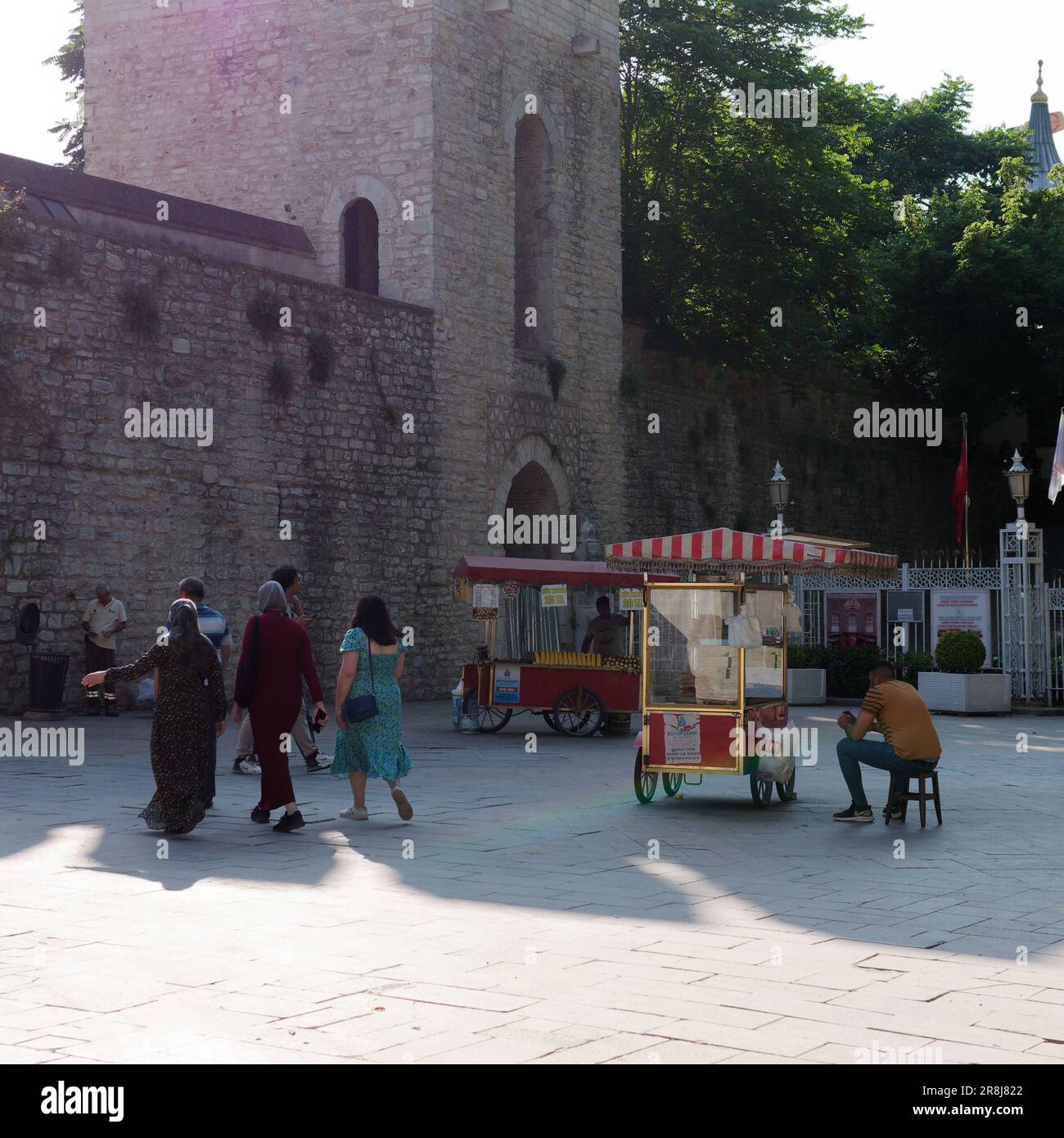 Vendeur assis à côté d'un chariot rouge vendant Simits aka bagels turcs par l'entrée de style forteresse construite en pierre Gulhane Park à Istanbul en Turquie Banque D'Images