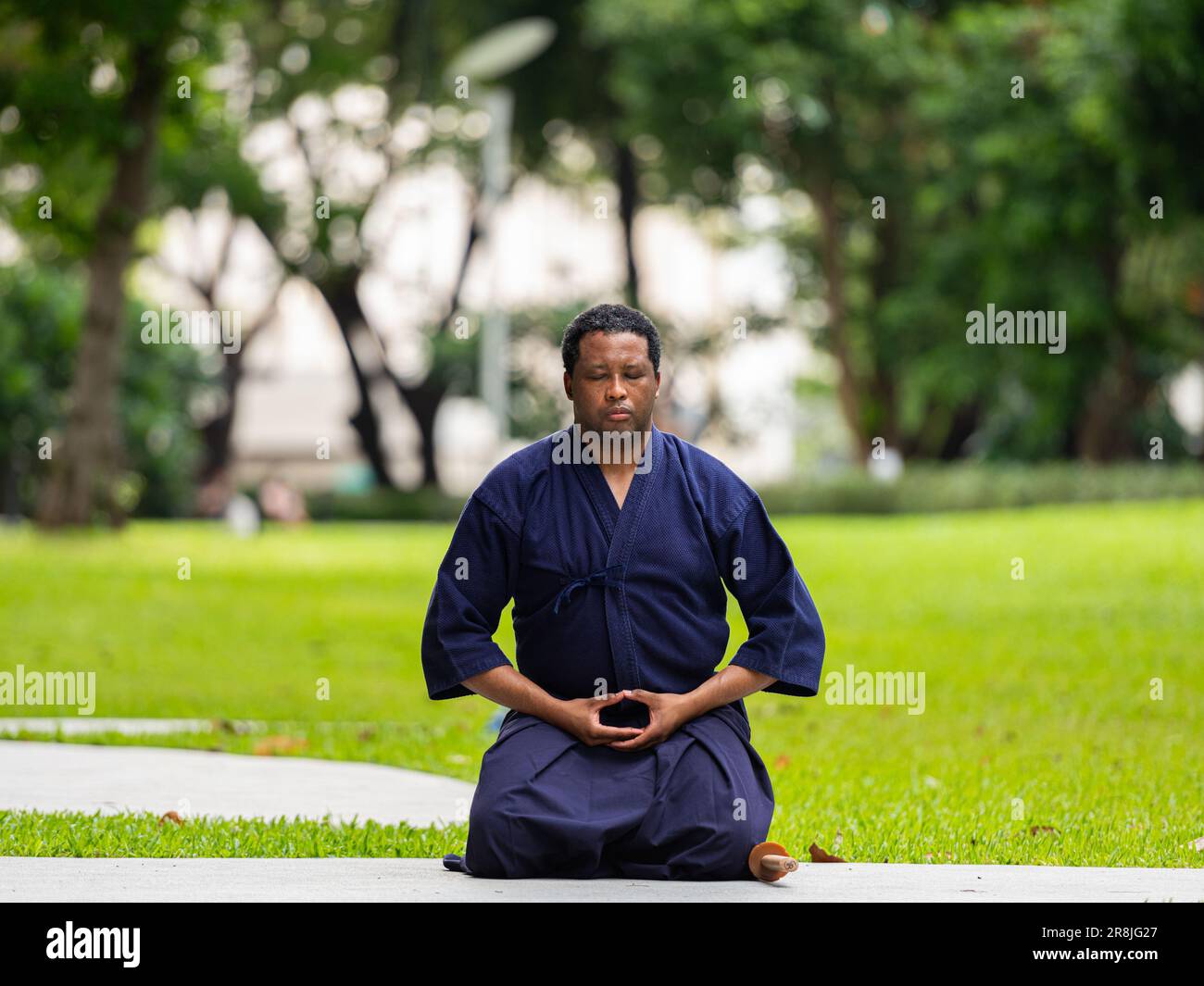 Portrait de beau noir artiste martial homme avec le costume d'arts martiaux de kendo faisant la méditation et le yoga au parc Banque D'Images