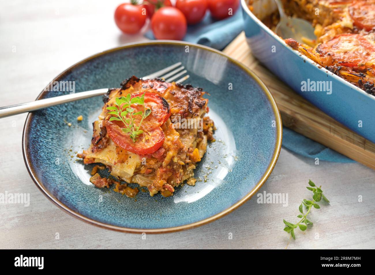 Partie de lasagne dans une assiette bleue, plat de cocotte avec couches de pâtes, sauce bolognaise, bœuf haché, légumes et tomates, recouvert de fromage fondu, c Banque D'Images