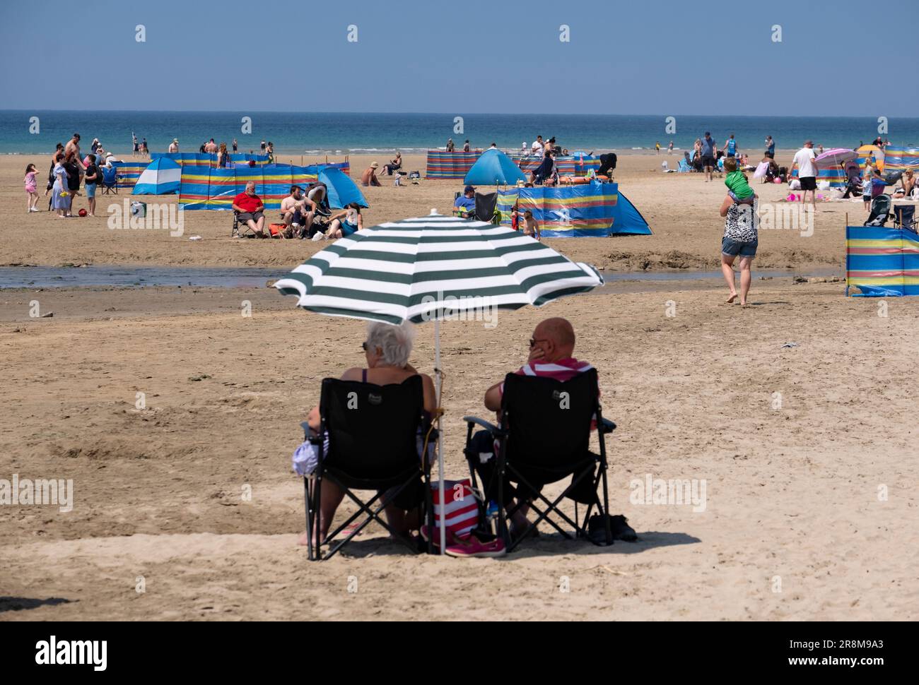 Les vacanciers profitent du soleil sur la plage de Peranporth, en Cornouailles, en Angleterre. Les brise-vent multicolores et les parapluies offrent un abri de la chaleur. Banque D'Images