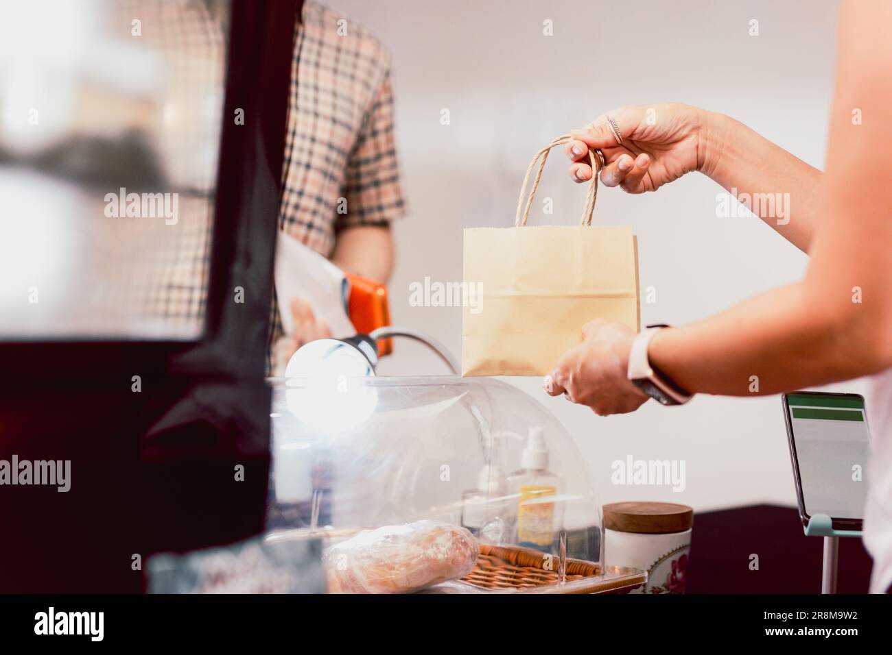 Serveuse au comptoir donnant des aliments dans un sac en papier au client pour les emporter. Banque D'Images