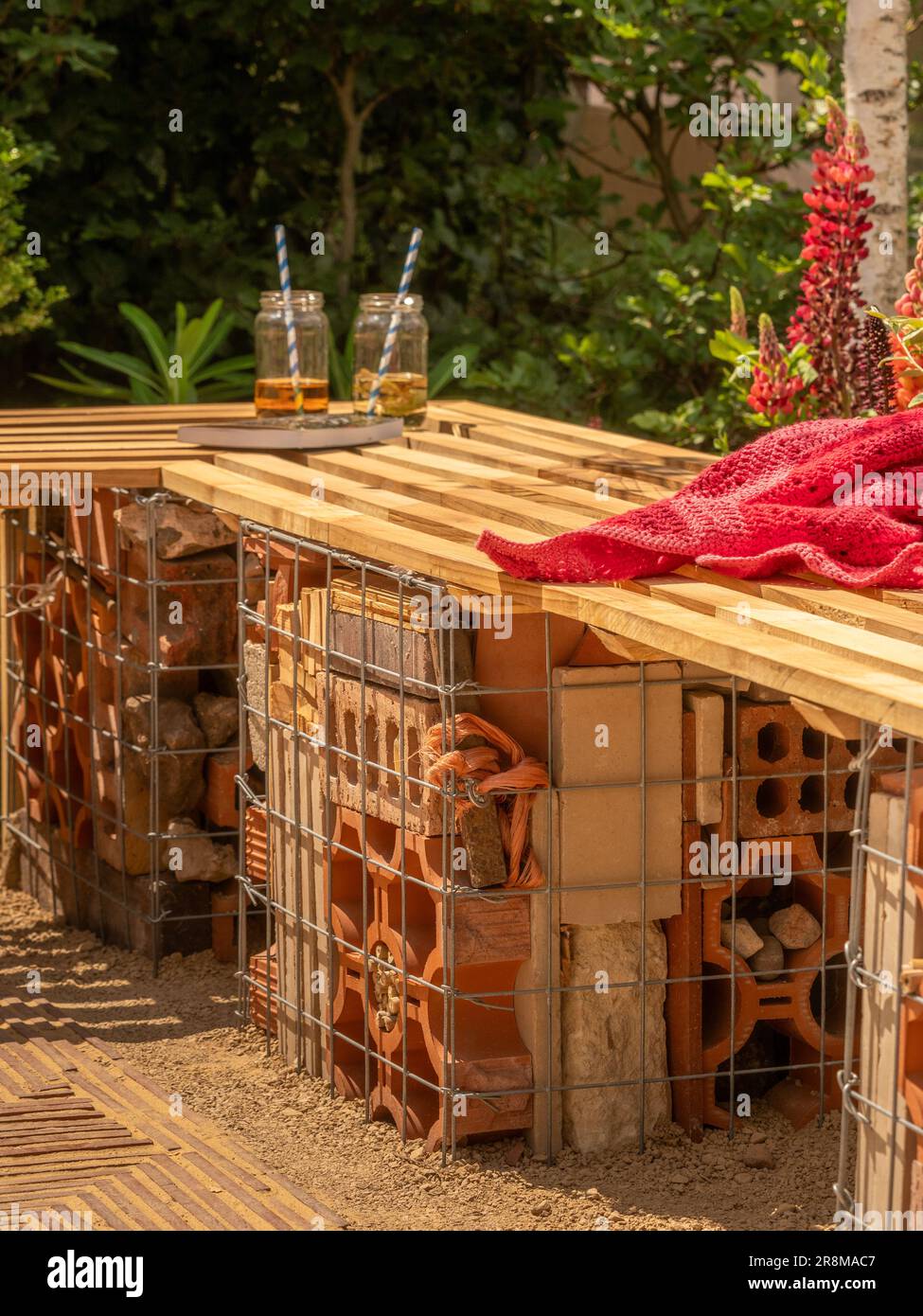 Banc de jardin à lattes en bois soutenu par des gabions en fil de fer remplis de briques dans un jardin d'exposition au Royaume-Uni exposition de jardin. Banque D'Images