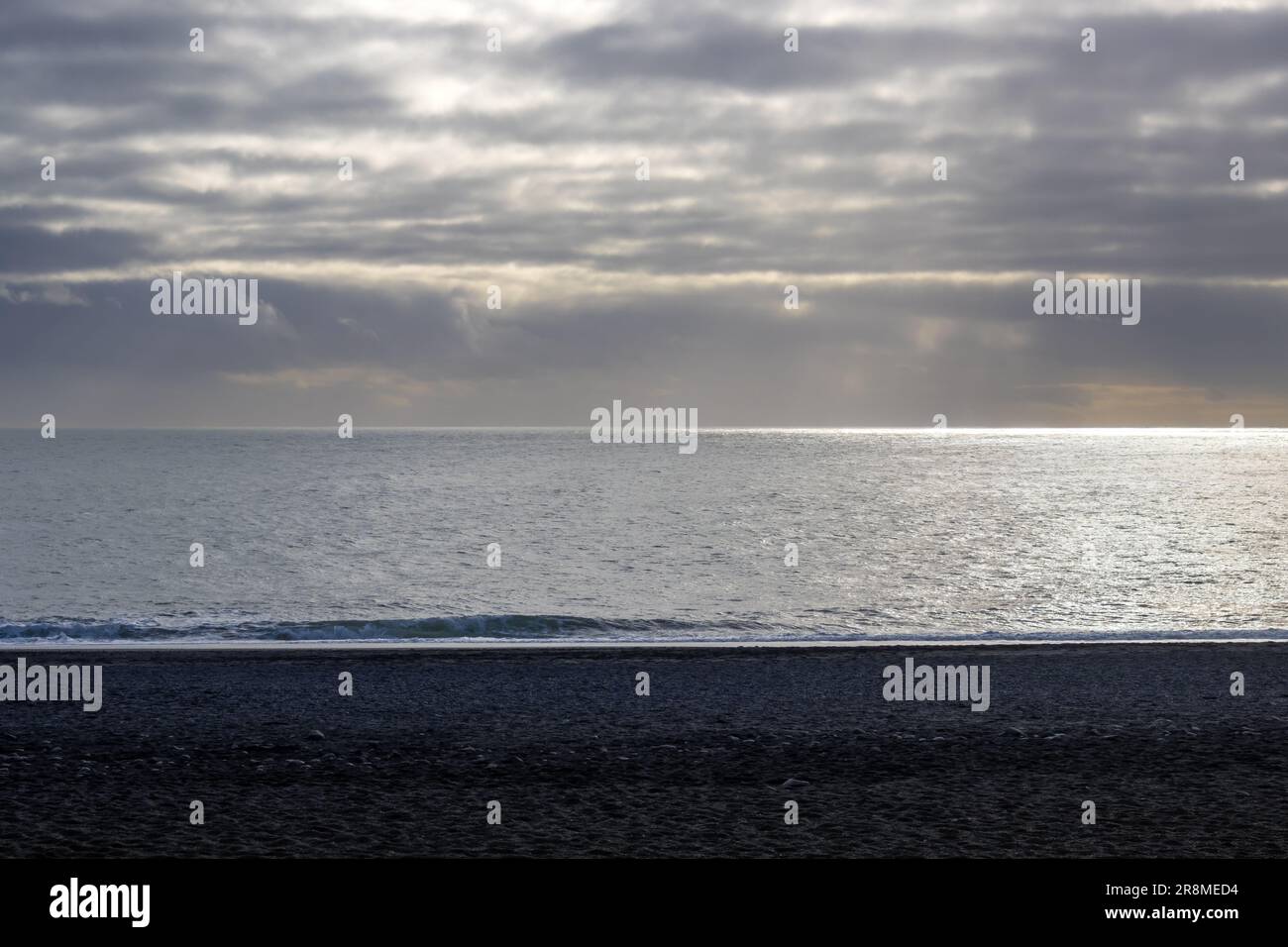 Plage et eau calmes. Horizon de l'océan Atlantique. Ciel nuageux d'automne avec une touche de lumière du soleil. Sable noir. Reynisfjara, sud de l'Islande. Banque D'Images