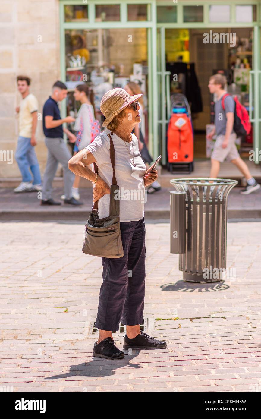 Femme âgée vêtue de façon décontractée tenant un téléphone portable regardant à distance - Tours, Indre-et-Loire (37), France. Banque D'Images