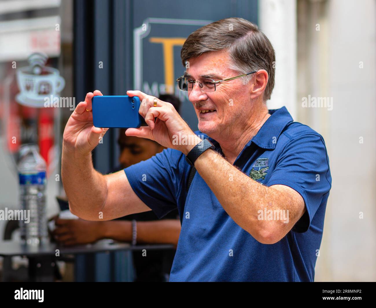 Homme souriant en bleu chemise et lunettes tenant le téléphone mobile prendre des photos - Tours, Indre-et-Loire (37), France. Banque D'Images