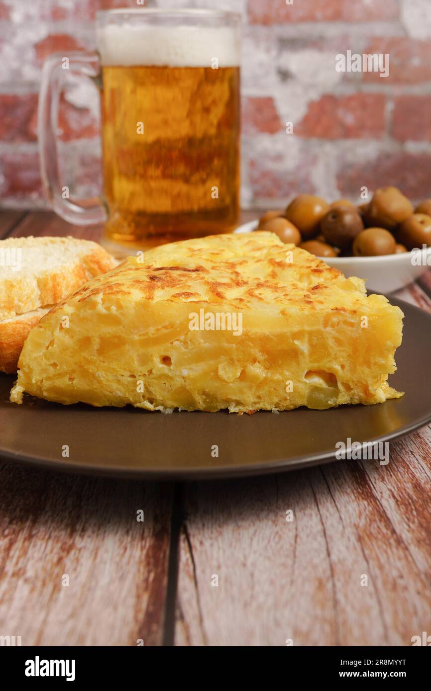 Omelette espagnole typique fraîchement préparée sur une table en bois avec un pichet frais de bière, couverts, pain et olives Banque D'Images