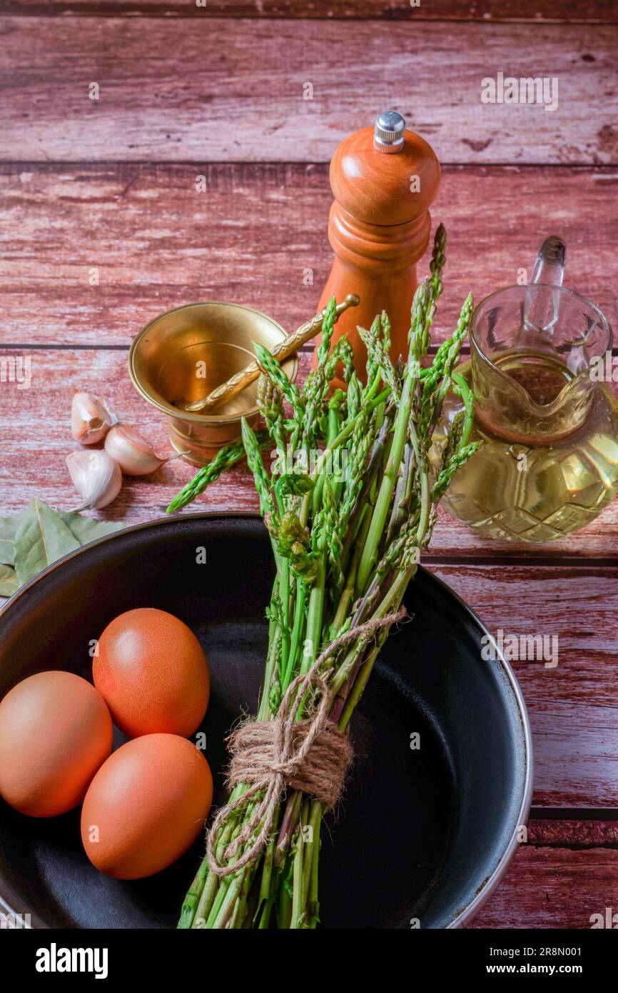 Bouquet d'asperges sauvages dans une poêle avec œufs, ail, huile d'olive et poivre, ingrédients pour faire une omelette Banque D'Images