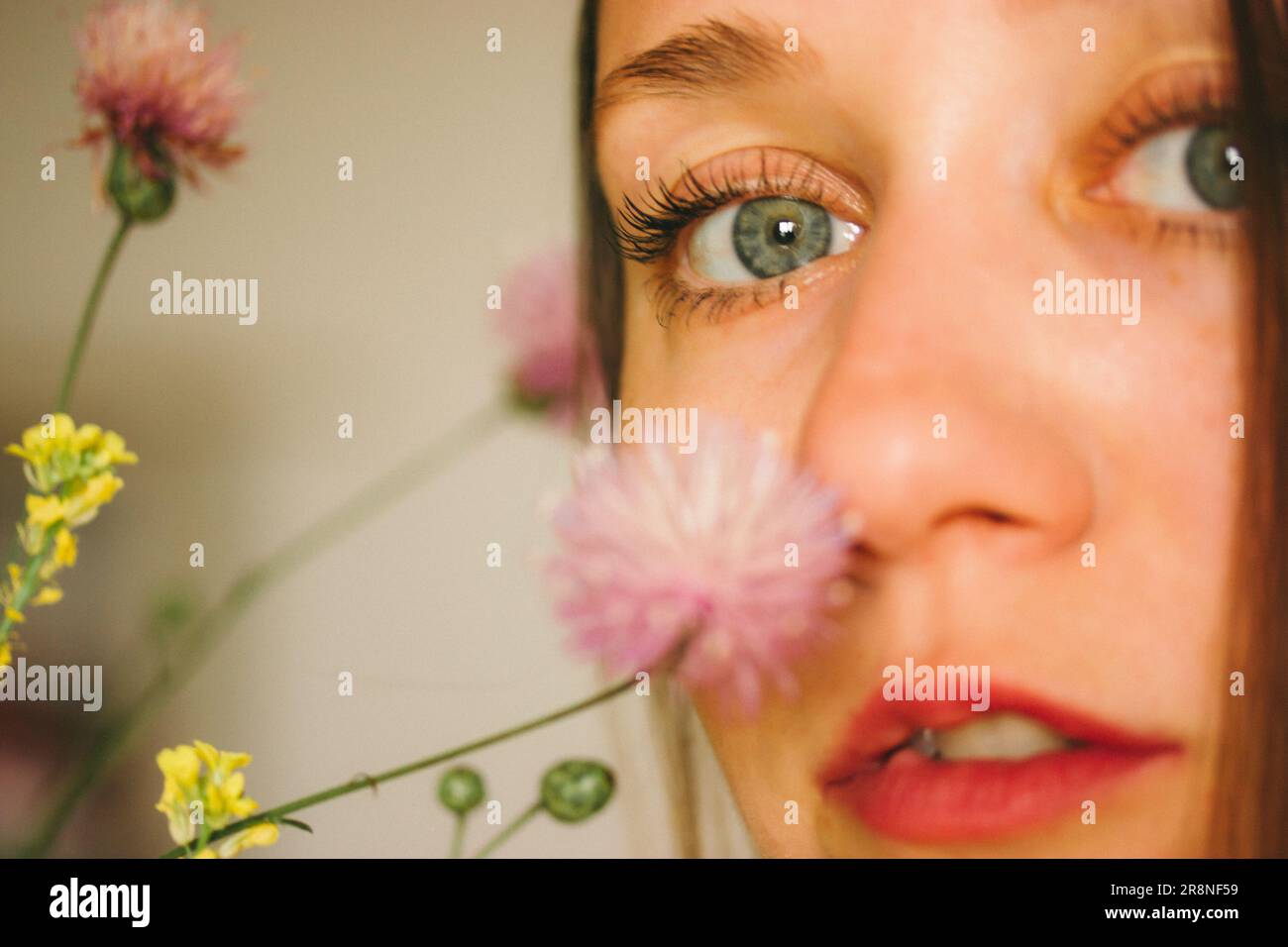 Belle jeune femme avec des yeux bleus renifler des fleurs sauvages fraîches dans un vase. Portrait de femme en gros plan. Macro photo de fleurs. Sel pour fille blanc aux yeux bleus Banque D'Images