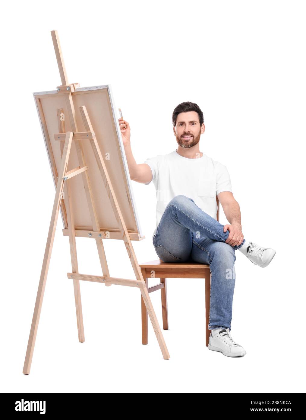 Joyeux homme peignant avec la brosse sur fond blanc. Utilisation du chevalet pour tenir la toile Banque D'Images