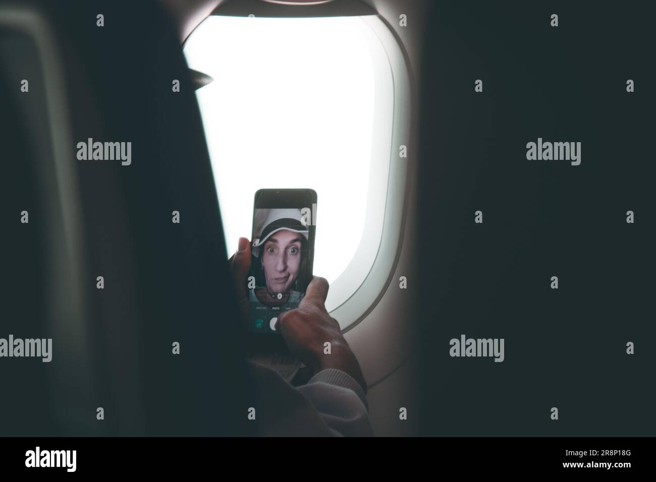 Jeune femme caucasienne pose passager pour selfie écran tactile smartphone dans le siège de cabine d'avion avant le vol. Drôle de filles sur le poste de vacances sur socia Banque D'Images
